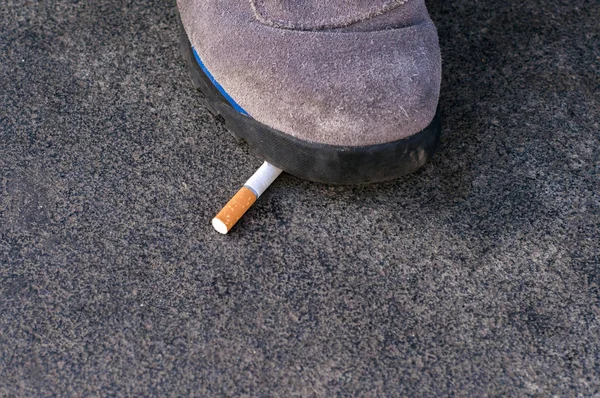 a man foot step on a cigarette to Quit Smoking - World tobacco day, Shoes crushing a cigarette butt on asphalt, Man refuses to smoking