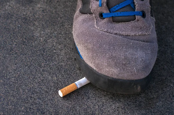 Ein Mann tritt auf eine Zigarette, um mit dem Rauchen aufzuhören - Welttabaktag, Schuhe zerquetschen einen Zigarettenstummel auf Asphalt, Mann weigert sich zu rauchen — Stockfoto