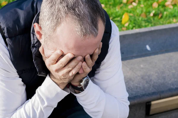 Businessman in depression with hands on forehead. stressed young business man, resting face on fist, isolated background of trees outside. Negative human emotion facial expression feelings.