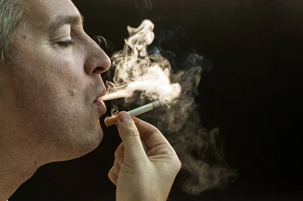 Mann raucht Zigarette auf schwarzem Hintergrund, schöner junger Mann raucht Zigarette, mysteriöser Mann mit Zigarre und Rauch isoliert auf schwarzem Hintergrund — Stockfoto