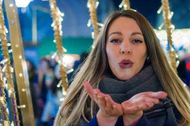 Genç gülümseyen kız öpücük üfleme Noel için dört gözle. Mutlu kadın üzerinde avuç içi öpücük sokak Noel backg karşı esen