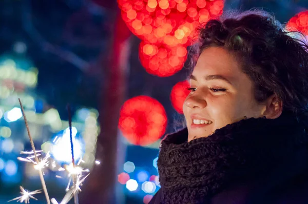 Sonriente adolescente en la calle por la noche con bengalas. Mujer joven sosteniendo una bengala encendida para celebrar el año nuevo — Foto de Stock