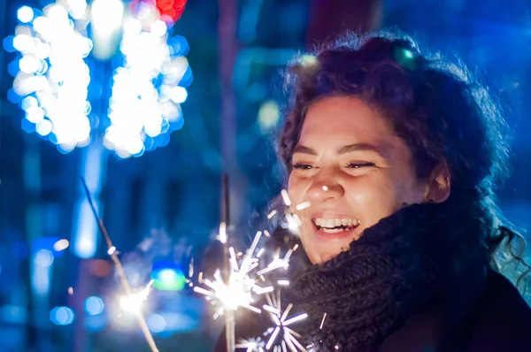 Joven chica sonriente sosteniendo chispa en su mano. Sonriente adolescente en la calle por la noche con bengalas — Foto de Stock