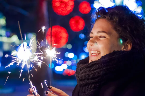 笑顔の女性は、新年のお祝いで線香花火を開催します。新年を祝うために点灯して線香花火を保持している若い女性 — ストック写真