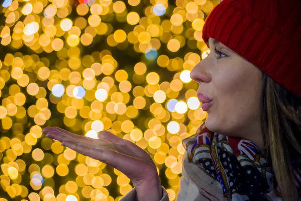 若い笑顔の女の子はキスを吹いてクリスマスを楽しみにして。近くで通りのクリスマス背景にキスを吹く女 — ストック写真