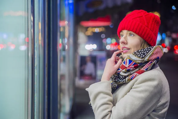 ウィンドウ ショッピングを楽しんでいる若い女性。店の窓に服を見て赤い帽子の女 — ストック写真