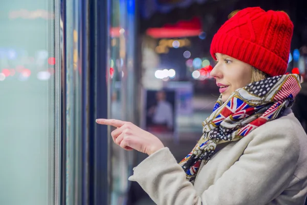 ショップのウィンドウ ショッピング バッグ ポインティング指を持つ女性。保管場所に入る前に店の窓を指して笑顔の女性 — ストック写真