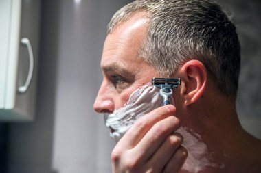 Yakışıklı adam banyoda sakalını tıraş. Aynanın önünde tıraş olgun yakışıklı adam. Cilt Bakımı.