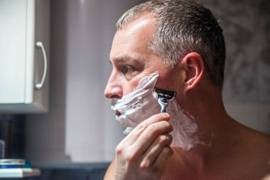 Yakışıklı adam banyoda sakalını tıraş. Aynanın önünde tıraş olgun yakışıklı adam. Cilt Bakımı.