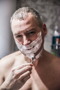 Yakışıklı delikanlı yüzünü tıraş ve aynaya bakıyor. Çıplak yakışıklı bir jilet kullanarak ve uzağa bakarak tıraş portresi