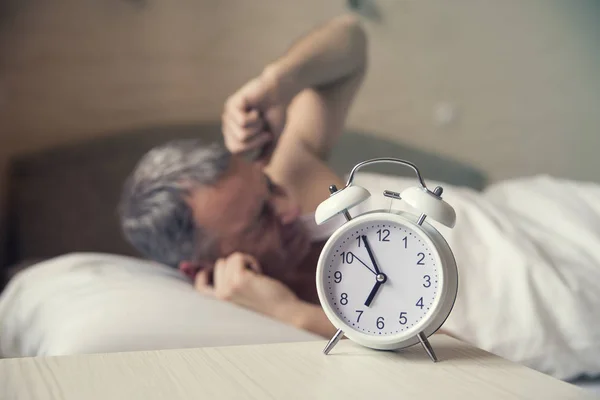 Sover man störd av väckarklockan tidigt på morgonen. Arg man i sängen vaknat av ett ljud. Vaknat upp. Mannen i sängen att stänga av en väckarklocka på morgonen vid 7 am — Stockfoto