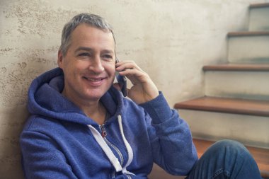 İyi haber paylaşımı. Yan görünüm yakışıklı genç adam cep telefonda konuşurken ve merdiven otururken gülümseyerek. Adam akıllı