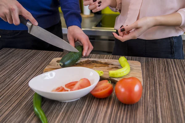 Pareja preparando verduras juntos en casa en la cocina. Primer plano de manos humanas cocinar ensalada de verduras en la cocina en la mesa de madera. Comida saludable y concepto vegetariano — Foto de Stock