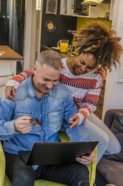 Pasangan bahagia menggunakan kartu kredit untuk berbelanja online dengan nyaman. Happy mixed-race couple shopping online — Stok Foto
