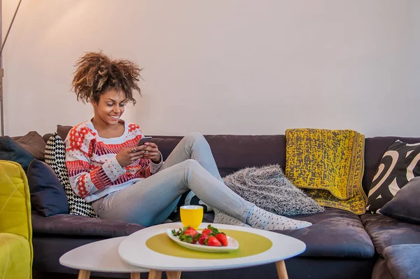 Femme heureuse à la maison lisant un message texte dans son salon lumineux. Jeune femme détendue messagerie texte sur canapé — Photo