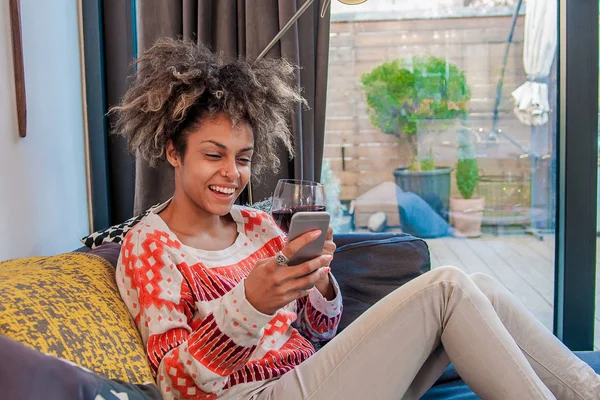 使用现代的智能手机设备的年轻时髦女孩虽然坐在家里和朋友在社会网络中，进行交流女性自由职业者，从家庭、 幸福和享受的生活方式工作 — 图库照片