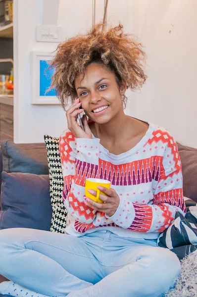 Temperamentvolle schöne junge afrikanisch-amerikanische Dame mit Afro-Frisur, die auf ihrem Handy plaudert und einem Anruf mit einem strahlenden Lächeln des Entzückens lauscht — Stockfoto