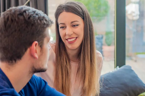 Porträtt av vackra unga par i casual kläder tittar på varandra och ler, sitter innan windows. Beskuren bild av vackra unga paret tittar på varandra — Stockfoto