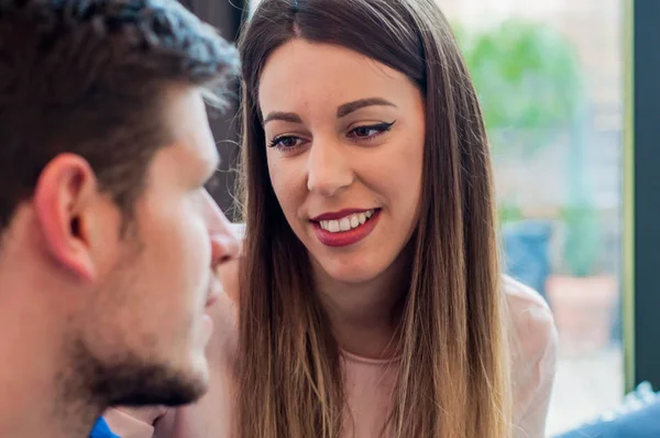 Retrato de una hermosa pareja joven con ropa casual mirándose y sonriendo, sentados ante las ventanas. Imagen recortada de hermosa pareja joven mirándose entre sí —  Fotos de Stock