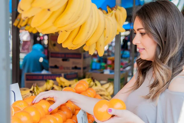 Positive young woman buying oranges on marketplace. woman choosing orange — Stock Photo, Image