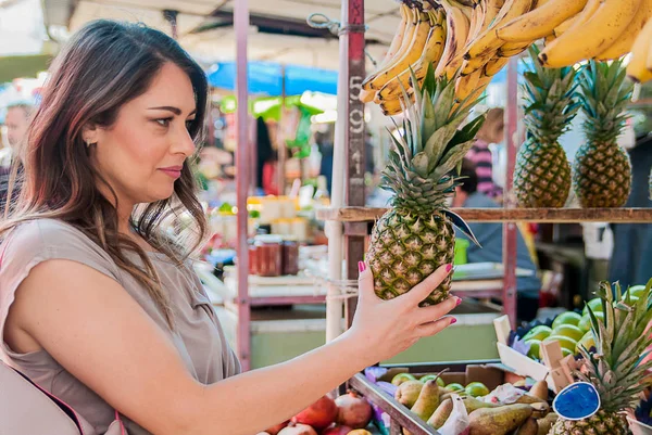 Attractive woman shopping in green market. Closeup portrait beautiful young woman picking up, choosing fruits, pineapples. Positive face expression emotion feeling healthy life style — Stock Photo, Image