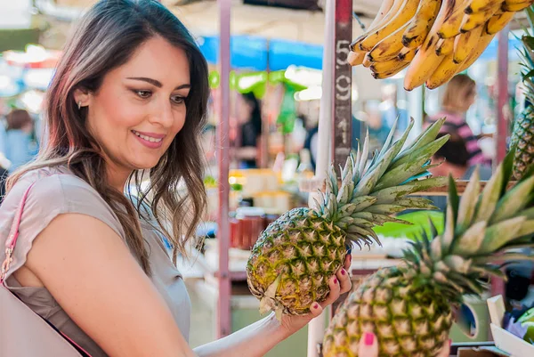 Woman choosing pineapple during shopping at fruit vegetable green market. Attractive woman shopping. beautiful young woman picking up, choosing fruits, pineapples. — Stock Photo, Image