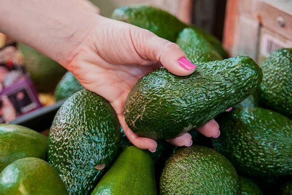 Обрізане зображення клієнта, який вибирає авокадо в супермаркеті. крупним планом жіноча рука тримає авокадо на ринку. продаж, покупки, їжа, споживання та концепція людей — стокове фото