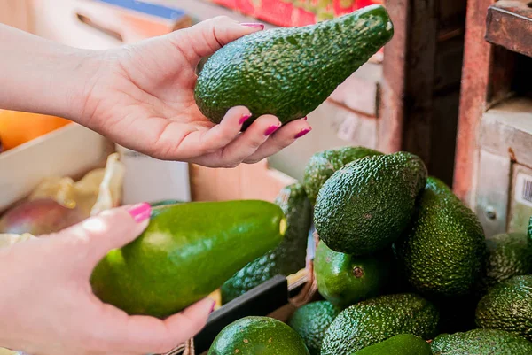Обрезанное изображение клиента, выбирающего авокадо в супермаркете. Закрыть женщину, держащую авокадо на рынке. продажа, шопинг, еда, потребительство и концепция людей — стоковое фото