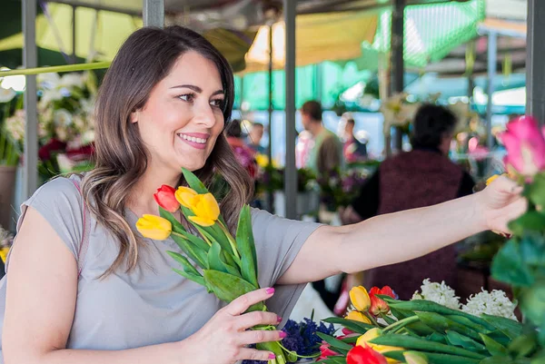 Mujer joven con hermoso ramo de tulipanes en el fondo de la tienda de flores. Retrato de una bonita hembra sonriendo mientras sostiene tulipanes frescos . — Foto de Stock