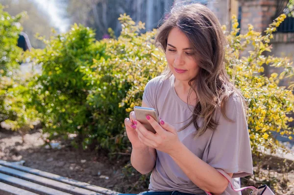 Un retrato de una hermosa mujer sonriente enviando mensajes con su teléfono. Mujer atractiva usando el teléfono celular al aire libre . — Foto de Stock