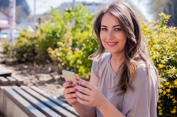 Yeşil odaklanmamış arka plana sahip bir parkta akıllı telefonda yazarak güzel bir kadın portresi. Neşeli kadın manifatura bir parkta onun smartphone ile — Stok fotoğraf