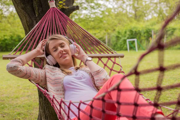 Close up portrait of woman lying down on hammock listening to music with cell phone.