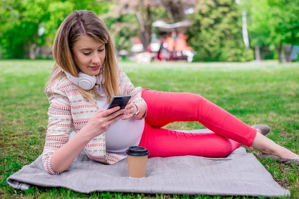 Ung kvinna liggande i färsk våren gräs Lyssna på musik på sin mobiltelefon — Stockfoto