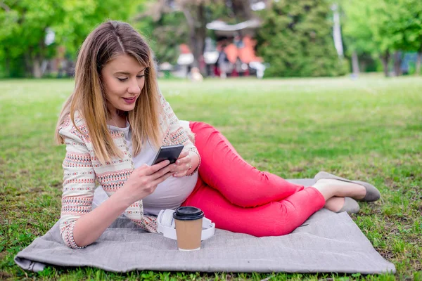 若い女性が彼女の携帯電話で音楽を聞きながら新鮮な春草に横たわって — ストック写真