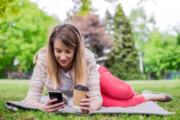 Retrato lateral de mulher rindo deitada na grama fora com telefone celular — Fotografia de Stock