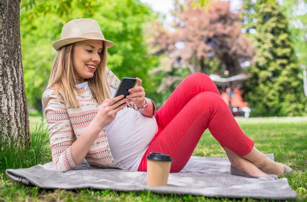 Porträtt av ung glad kvinna liggande på gräset håller mobiltelefon — Stockfoto