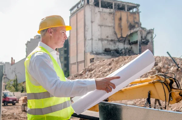 civil engineer working with documents on construction site. Construction engineer in yellow hardhat inspecting blueprints on building site