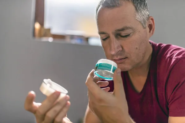 Mature man smelling cosmetic product. Handsome middle aged man holding container with cream