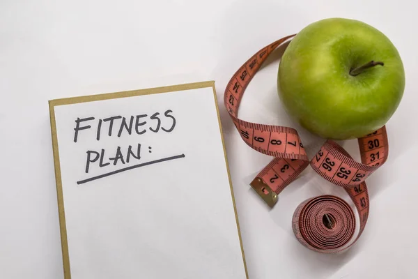 fitness plan note in notepad. Measuring tape, notepad and fresh green apple