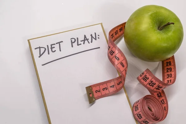 Diet plan note in notepad. Measuring tape, notepad and fresh green apple