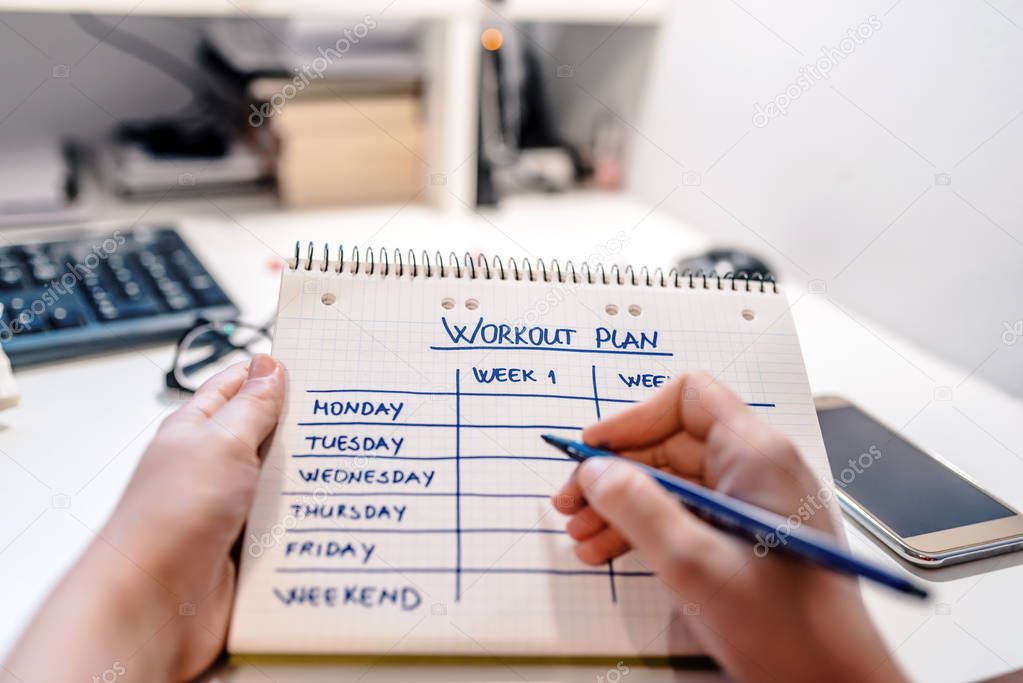 Closeup of male hands writing workout plan in checkered notebook. Planning and management concept 