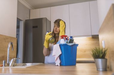 Lastik eldiven ve önlük sepeti ile temizlik malzemeleri mutfak önünde tutan sinir bozucu kadın. Mutsuz kadın temizlik büyük mutfak. genç çekici üzgün ve depresyonda kadın veya temizlik ev kadını. Yorgun ve çaresiz tembel ev ödevi ve kubbe
