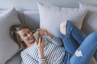 Kız bir akıllı telefon olarak çıkıyor. Mutlu kadın kanepede istimal hareket eden telefon. Mutlu kadın evde onun parlak oturma bir kısa mesaj okuma. Kanepede rahat genç kadın mesaj