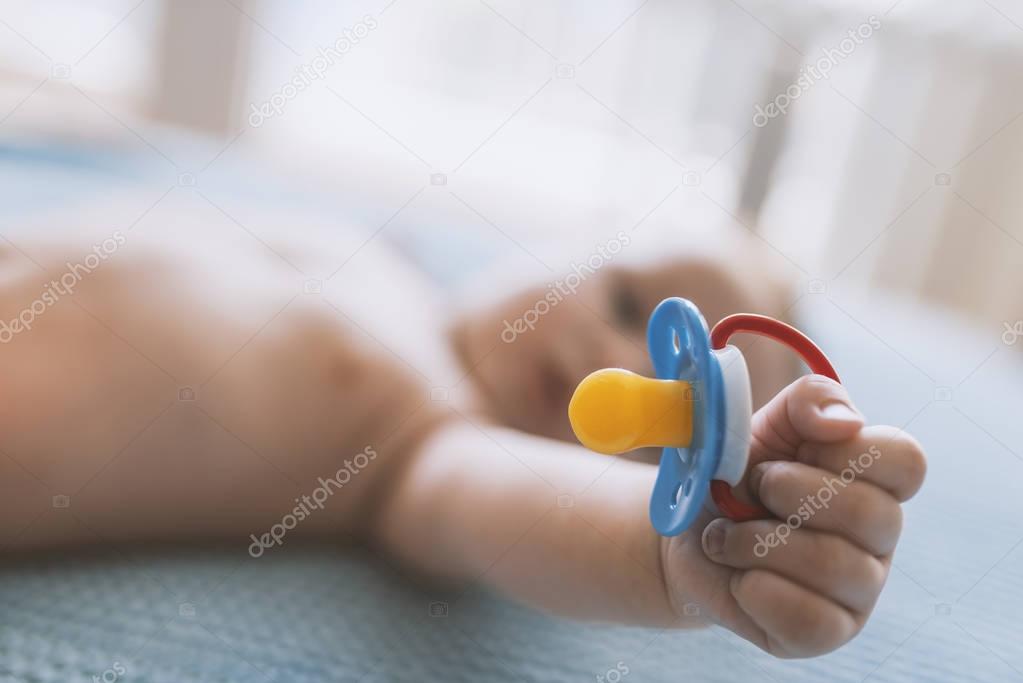 Baby with a nipple. Close up of baby hands with pacifier. Focus is on hands. Newborn sleeping on a blanket holding a pacifier in his hand. Baby is lying happy holding baby nipple soother in hand