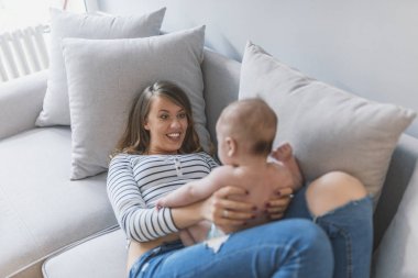 Oynamak, öğrenmek ve birlikte büyümek. Genç anne bebek oğlu ile evde oynarken. Anne bebekle oynarken. Mutlu anne sarılma şirin bir bebek yatakta portresi. Güzel genç anne şirin bebeği ile oynama ve gülümseyen