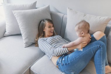 Oynamak, öğrenmek ve birlikte büyümek. Genç anne bebek oğlu ile evde oynarken. Anne bebekle oynarken. Mutlu anne sarılma şirin bir bebek yatakta portresi. Güzel genç anne şirin bebeği ile oynama ve gülümseyen