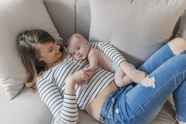 Yeni doğmuş çocuğunu tutan genç anne. Kadın ve yeni doğan çocuk rahatlayın. Evde aile. Mutlu anne ve bebek portresi. Şirin küçük bir çocuk ile yatakta yatan genç güzel anne.