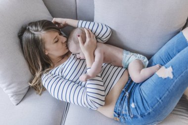 Yeni doğmuş çocuğunu tutan genç anne. Kadın ve yeni doğan çocuk rahatlayın. Evde aile. Mutlu anne ve bebek portresi. Şirin küçük bir çocuk ile yatakta yatan genç güzel anne.