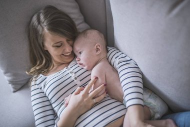 Yeni doğmuş çocuğunu tutan genç anne. Kadın ve yeni doğan çocuk rahatlayın. Evde aile. Mutlu anne ve bebek portresi. Şirin küçük bir çocuk ile yatakta yatan genç güzel anne.