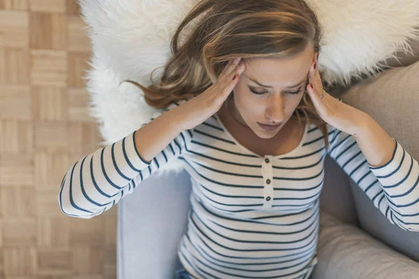 Woman with headache. Housewife woman in a couch with headache and a hand on forehead. Beautiful young woman portrait Headache depression stressed tired